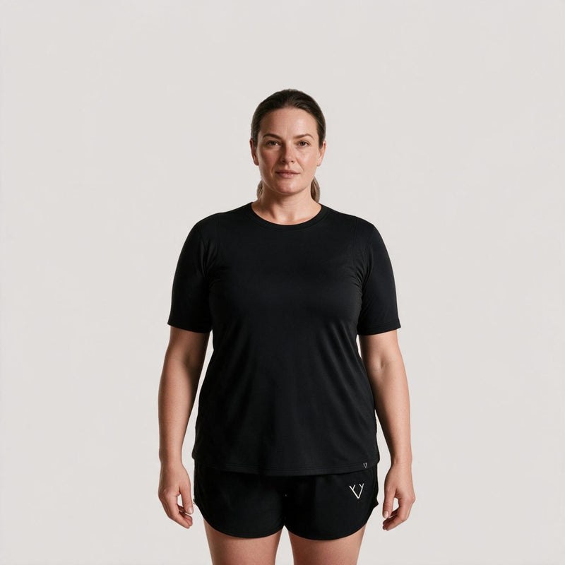 A woman modeling a black short-sleeve athletic t-shirt and matching black shorts against a light gray studio background.