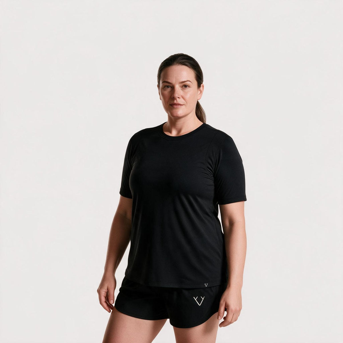 A woman modeling a black short-sleeve athletic t-shirt and matching black shorts against a plain light gray studio background.